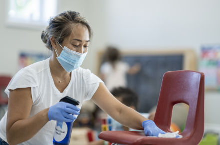 Teacher wearing mask spraying and wiping down chair