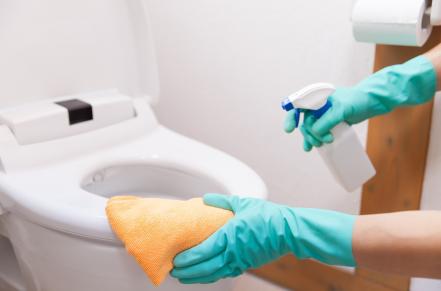 Gloved hands disinfecting toilet seat