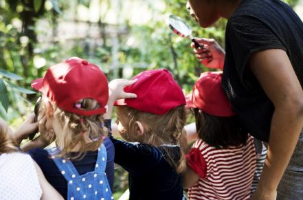 Children with matching red hats and their teacher looking at a garden