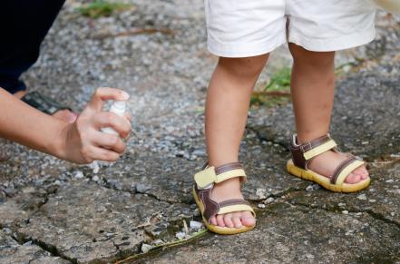 Adult hand spraying mist on to child's legs and feet