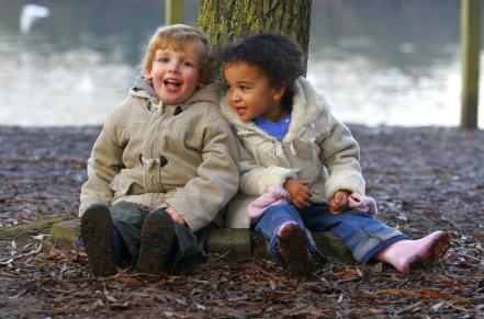 Two kids bundled up sitting under a tree