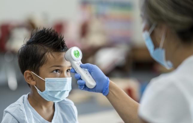 Masked provider using touchless thermometer to check masked child's temperature