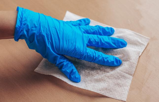 Gloved hand cleaning surface with paper towel