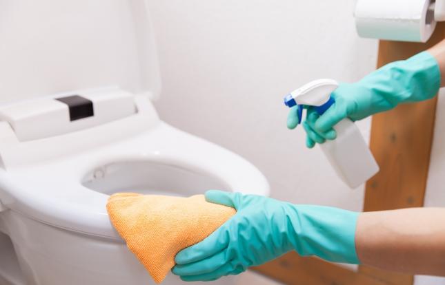 Gloved hands disinfecting toilet seat