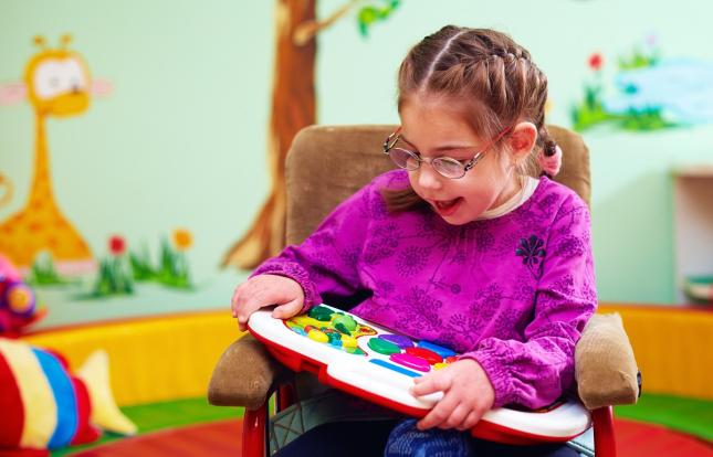 Child with special needs sitting in wheelchair playing with toy