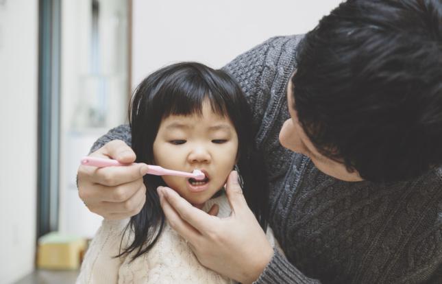 adult brushing child's teeth