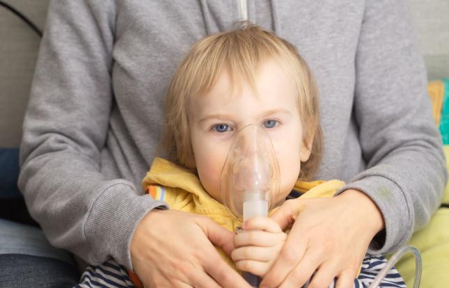 Child with nebulizer over their nose and mouth being embraced by adult